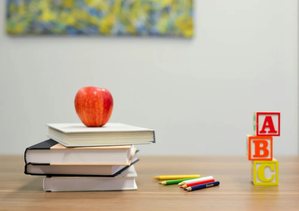 Books, coloured pencils, alphabet blocks, and an apple on a learning table